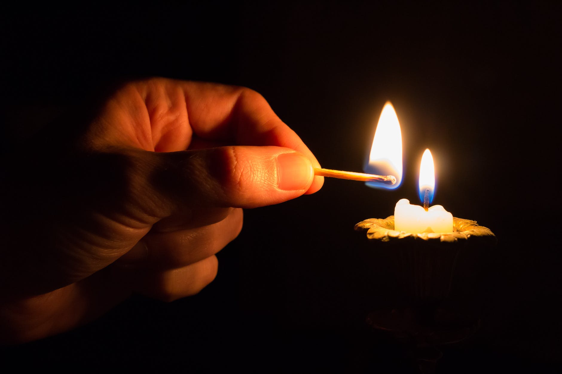 person holding match stick with fire in front of candle with fire