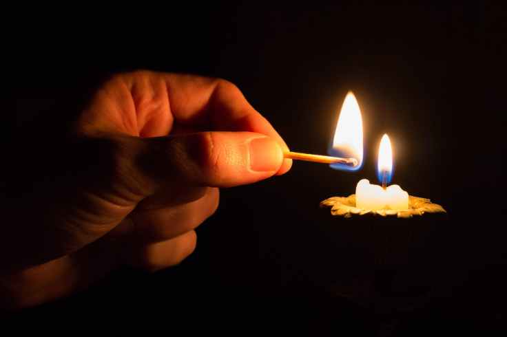 person holding match stick with fire in front of candle with fire